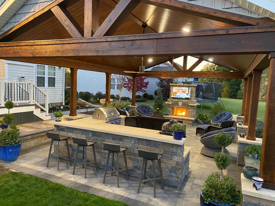 Covered outdoor living pavilion with stone bar, fireplace, seating, and television